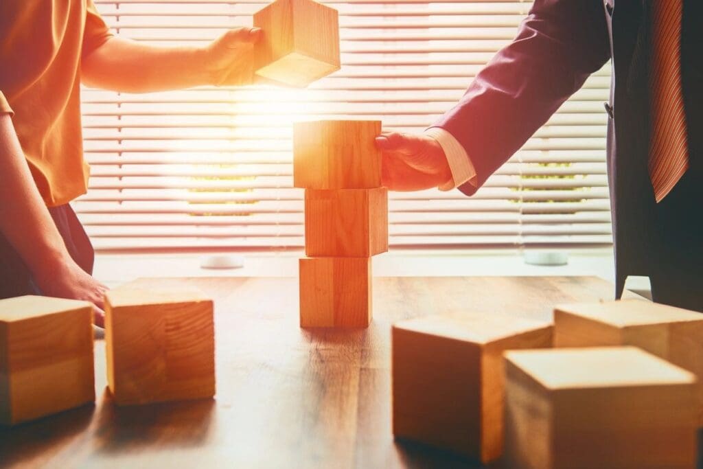 Two people are stacking blocks on top of a table.