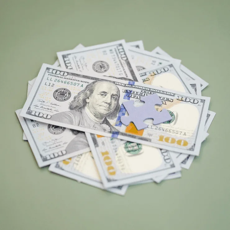 A pile of money with the shape of a puzzle piece on top.