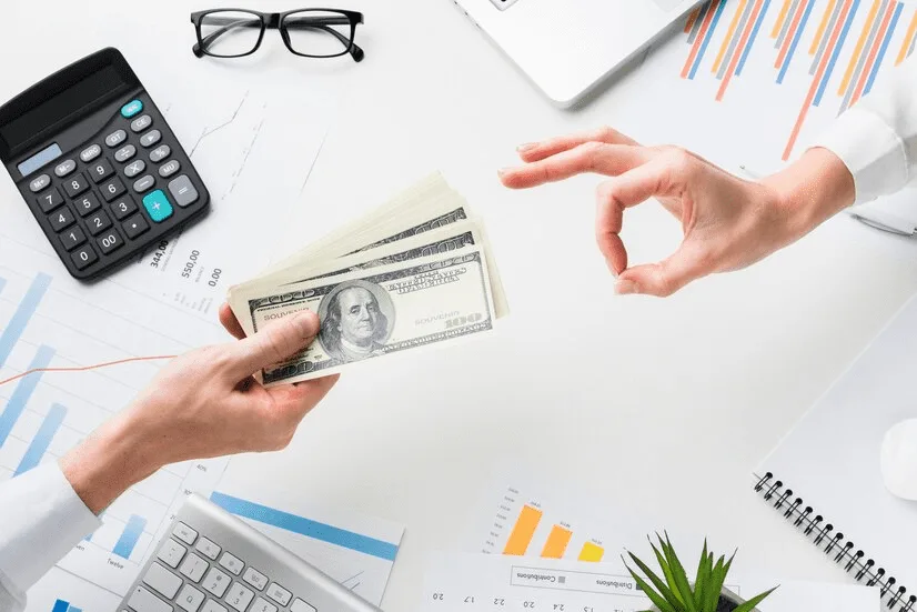 A person holding money in their hands over a desk.