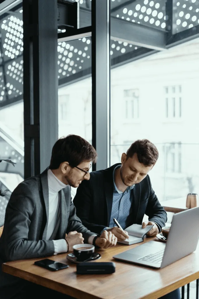 Two men in suits are looking at a laptop.