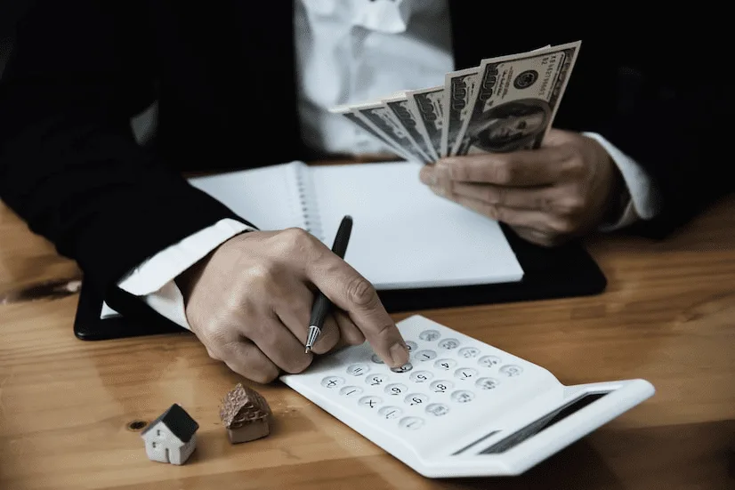 A person holding money and pointing to a calculator.