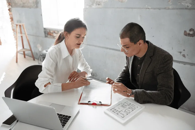 A man and woman sitting at a table with laptops.