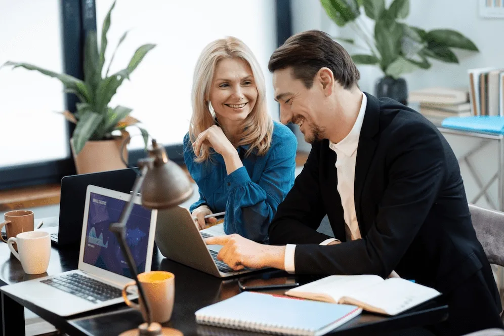 Two people sitting at a table with laptops