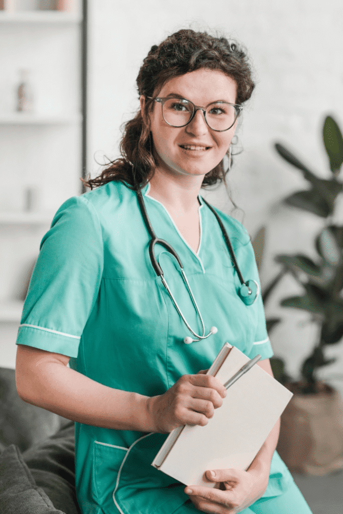 A woman in glasses and scrubs holding papers.