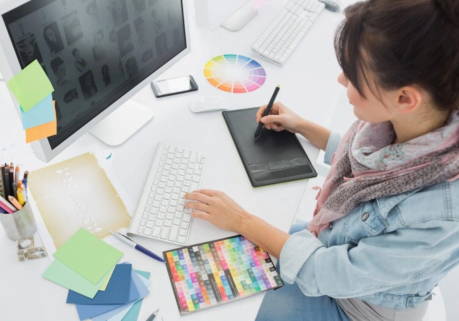 A woman using a tablet and computer on top of a desk.