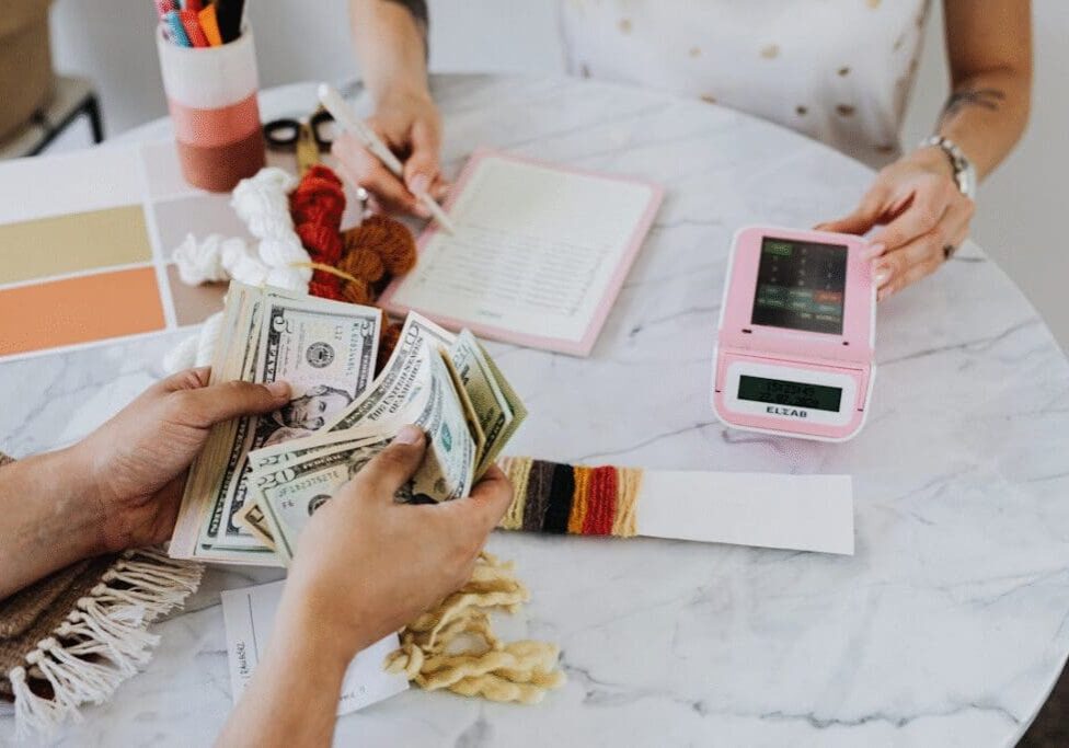 A person sitting on table and calculating and another counting dollar bills